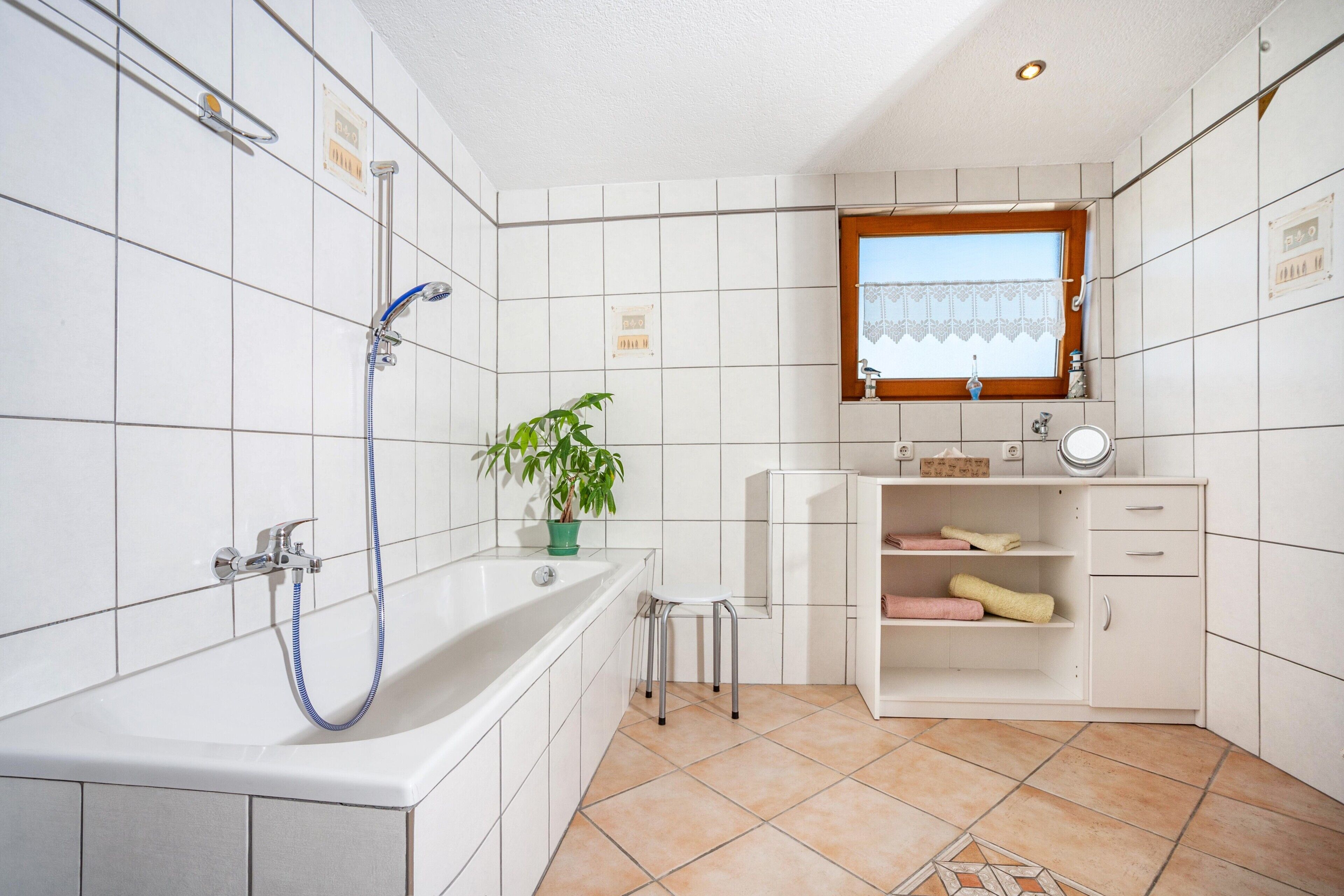 Un bagno con vasca, doccia, lavandino, specchio, finestra e una pianta in vaso.