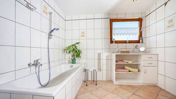 Un bagno con vasca, doccia, lavandino, specchio, finestra e una pianta in vaso.