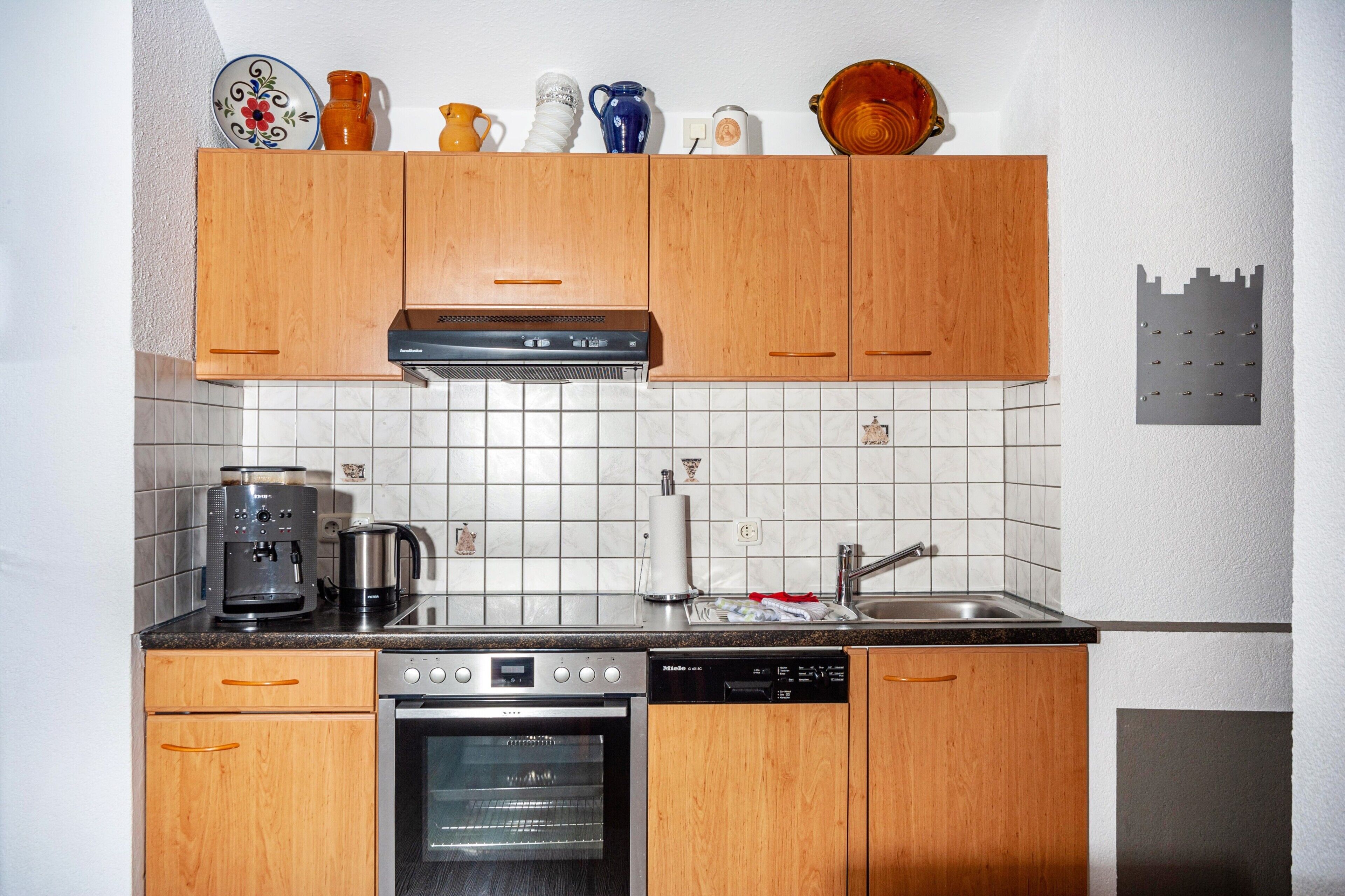 Eine kompakte Küche mit Holzschränken, einer Kaffeemaschine, einem Backofen und einem Geschirrspüler.
