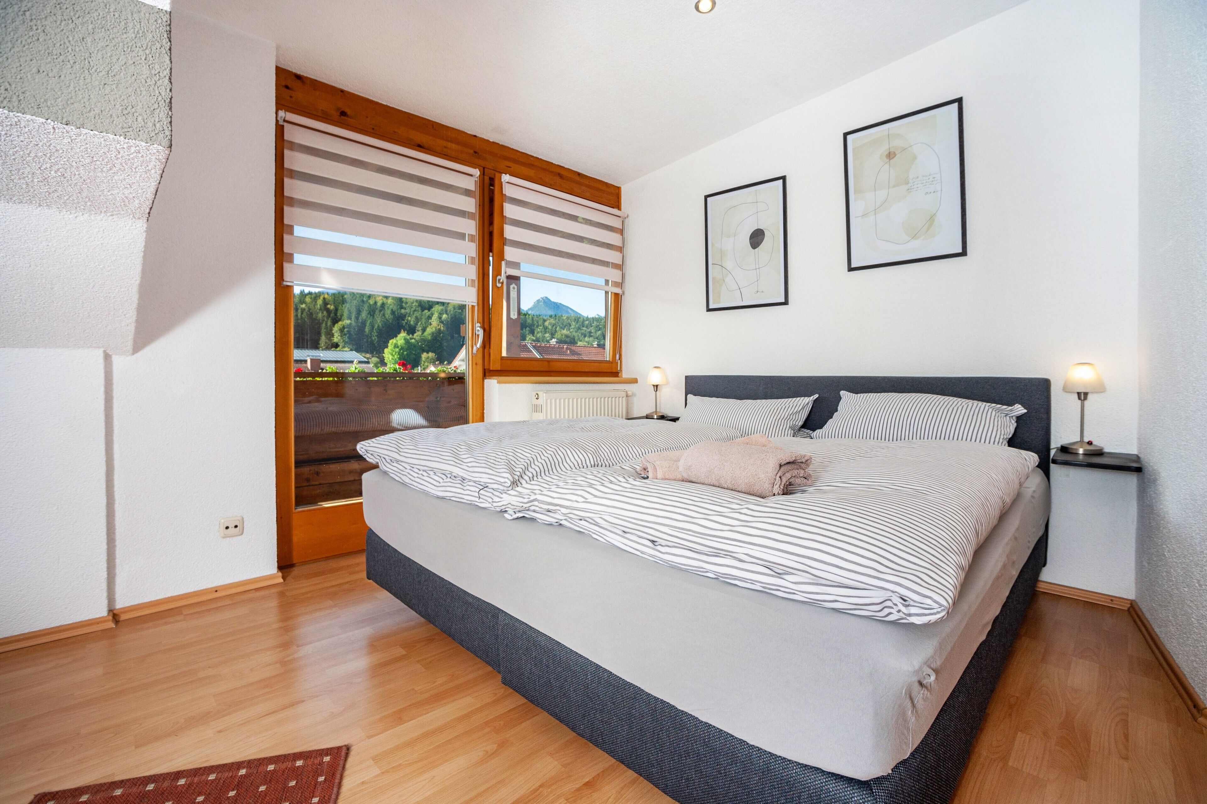 A bedroom with a bed, a window with blinds, a radiator, and a framed picture on the wall.