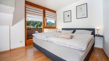 A bedroom with a bed, a window with blinds, a radiator, and a framed picture on the wall.