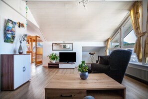 A modern living room with a wooden coffee table, a flat-screen TV, a dark sofa, and a potted plant. - Holiday Apartment "Paulas Koenigscard" with Mountain View, Balcony and Wi-Fi (Füssen)