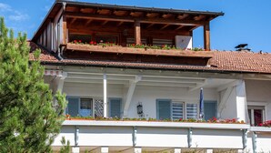 Un bâtiment à deux étages doté d’un balcon en bois, d’un toit recouvert de tuiles et d’une façade blanche.