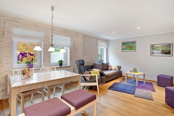 A modern living room with a dining area, a sofa, a small table, and a window with a view.
