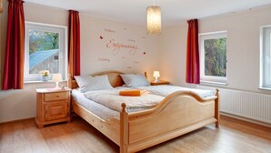 A bedroom with a wooden bed, two bedside tables, a window with curtains, and a wall with motivational words.