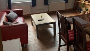 Ett vardagsrum med en röd soffa, ett soffbord i trä, en tv på ett träställ och utsikt över en gul byggnad genom stora fönster.