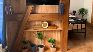 Ett rum med en tv som är monterad på en hylla av trä, en klocka och krukväxter.