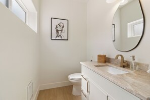 A modern bathroom with a white toilet, a sink with a marble countertop, a large mirror, and a framed artwork on the wall. - Modern Downtown Talent Dream (Talent)