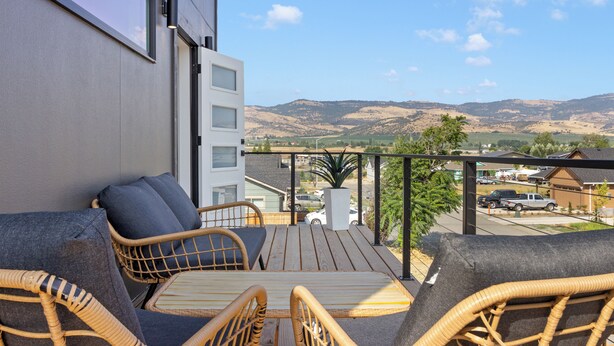 A balcony with wicker furniture, a view of a parking lot, and distant hills. - Modern Downtown Talent Dream (Talent)