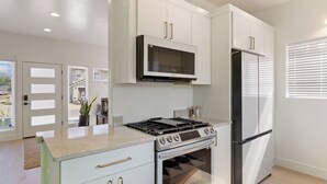 A modern kitchen with white cabinetry, a built-in microwave, a gas stove, and a stainless steel refrigerator. - Modern Downtown Talent Dream (Talent)