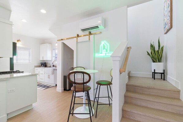 A modern kitchen with white cabinets, a dining area with two stools, and a staircase leading to another level.