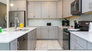 A modern kitchen with grey cabinets, stainless steel appliances, and a white countertop. - Wonderful 6bd 5bat w Golf Course Championsgate (Kissimmee)