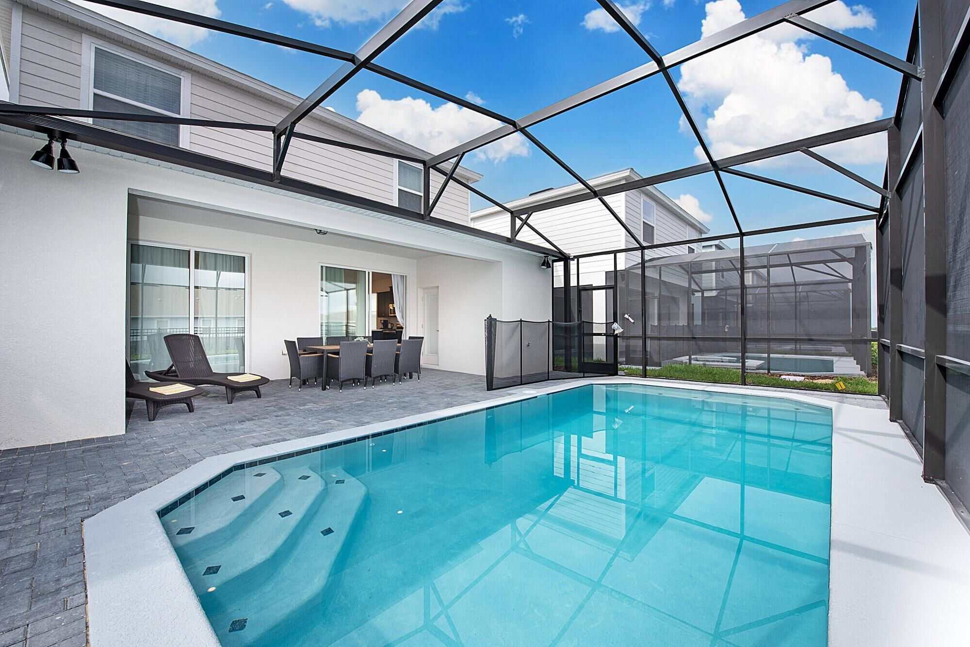 Ein moderner, überdachter Innenpool mit Glasdach, umgeben von einer Terrasse mit Sitzgelegenheiten und einem kleinen Tisch.