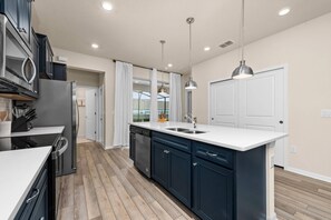 A modern kitchen with dark cabinets, a white countertop, and a built-in dishwasher. - Brand New Windsor Island 5 Suites (Davenport)