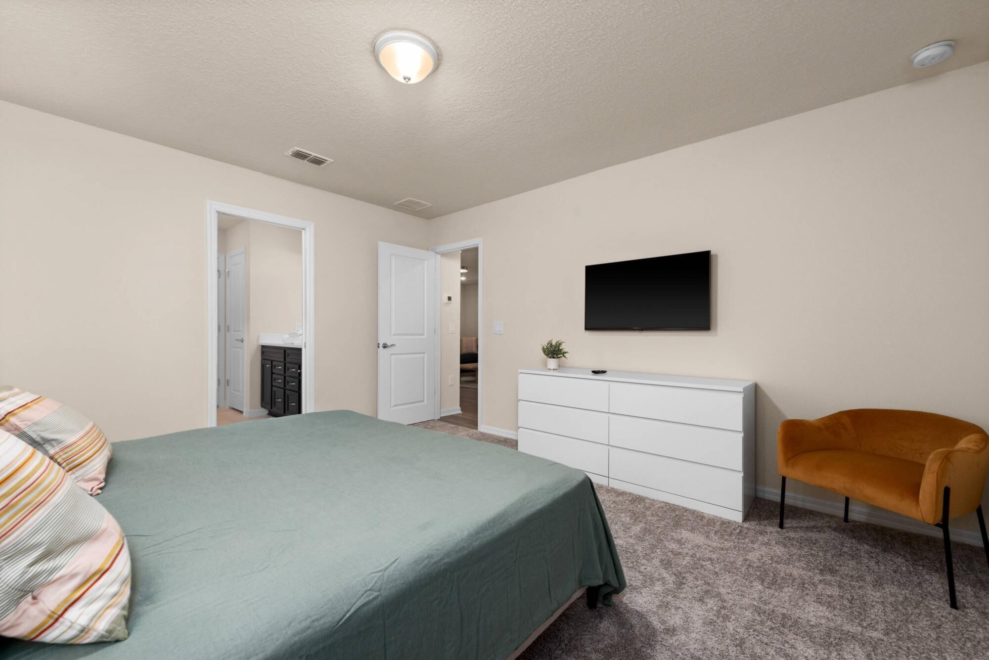 A bedroom with a bed, a dresser, a TV, and a chair.