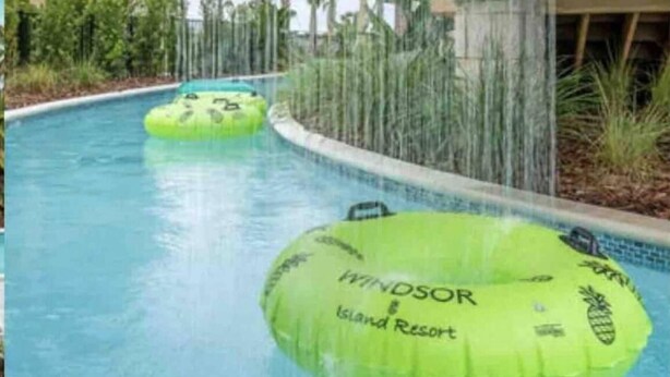 A pool area with two green inflatable tubes and a waterfall feature. - Brand New Windsor Island 5 Suites (Davenport)