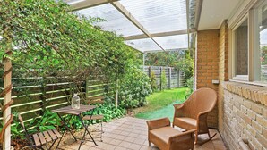 Une terrasse couverte, dotée d’une table et de chaises, entourée de verdure et bordée d’un mur de briques.