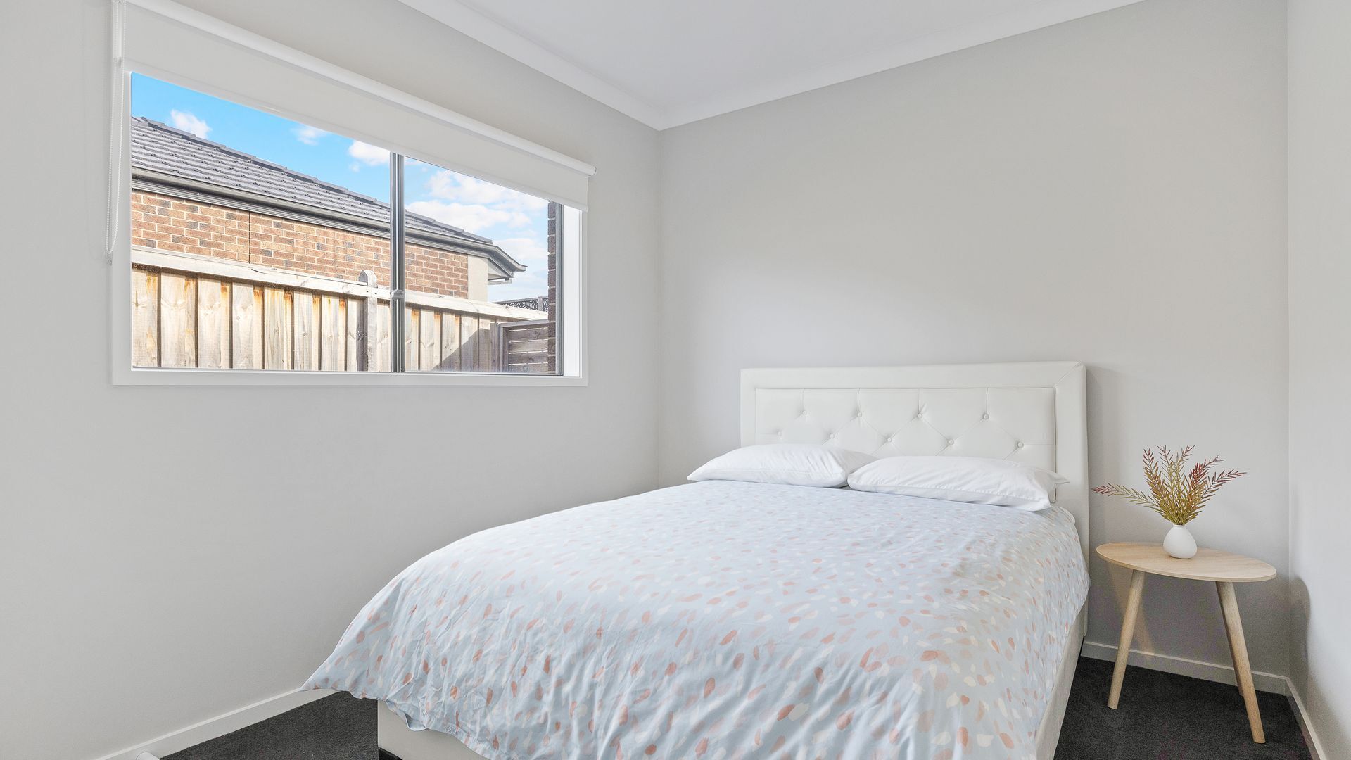 A bedroom with a bed, a window, and a small table with a vase.