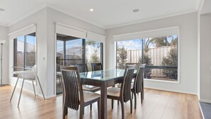 A modern dining area with a glass table and wooden chairs, large windows offering views of the backyard. - Seagrove Getaway in Cowes (Cowes)