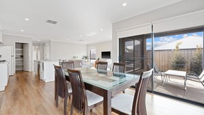 A modern kitchen with white cabinetry, a dining area with a glass table, and a large sliding glass door leading to an outdoor patio. - Seagrove Getaway in Cowes (Cowes)