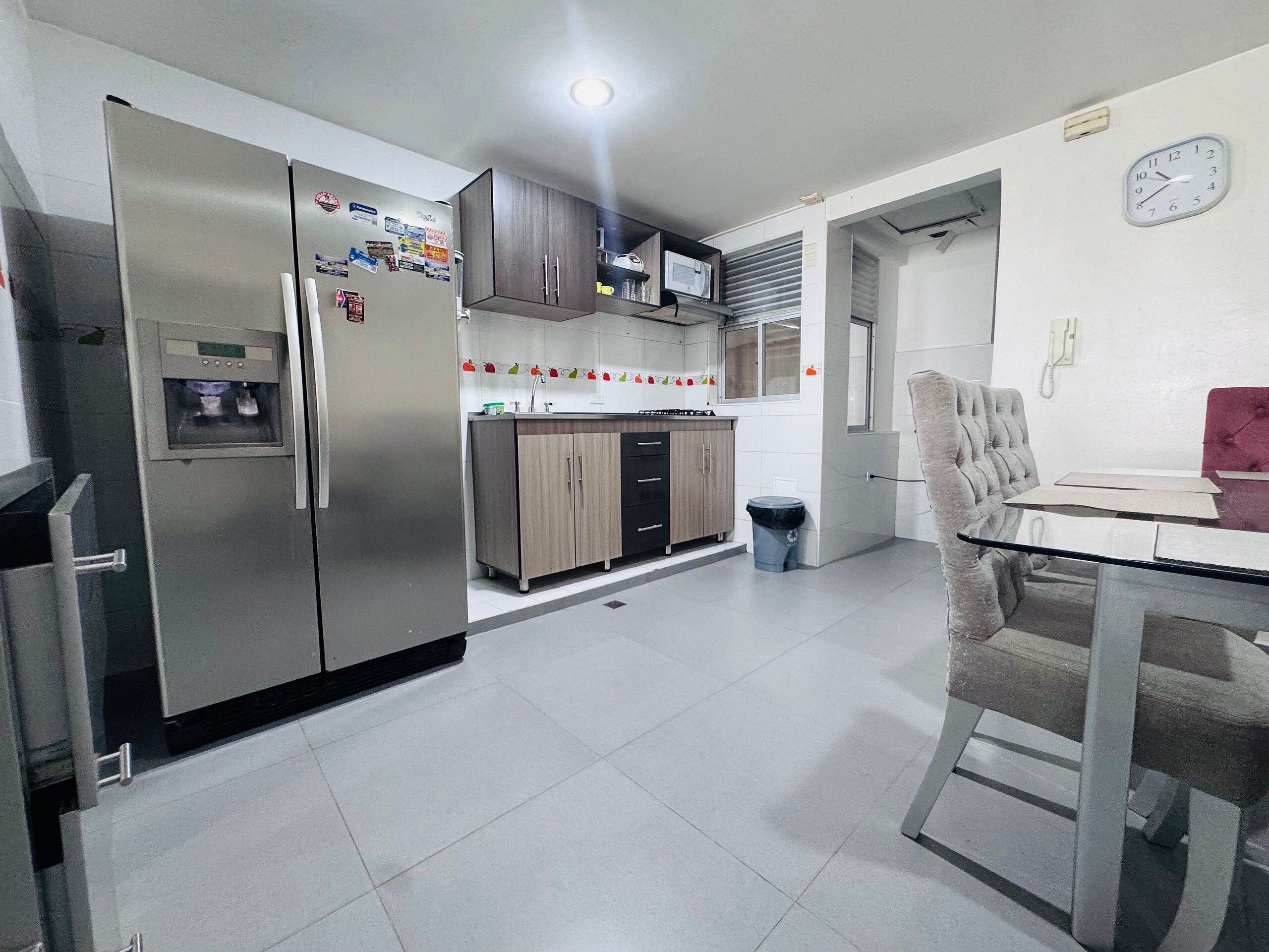 Una cocina moderna con refrigerador, gabinetes, microondas y una zona de comedor con mesa y sillas.