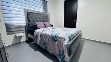 Un dormitorio con cama, ventana con persianas, una puerta y un equipo de aire acondicionado.