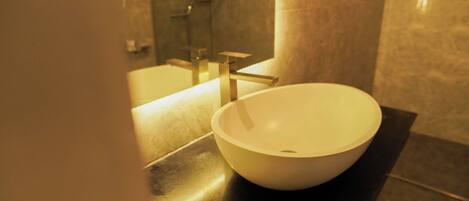 A modern bathroom with a large white vessel sink, a sleek vanity, and a glass-enclosed shower.