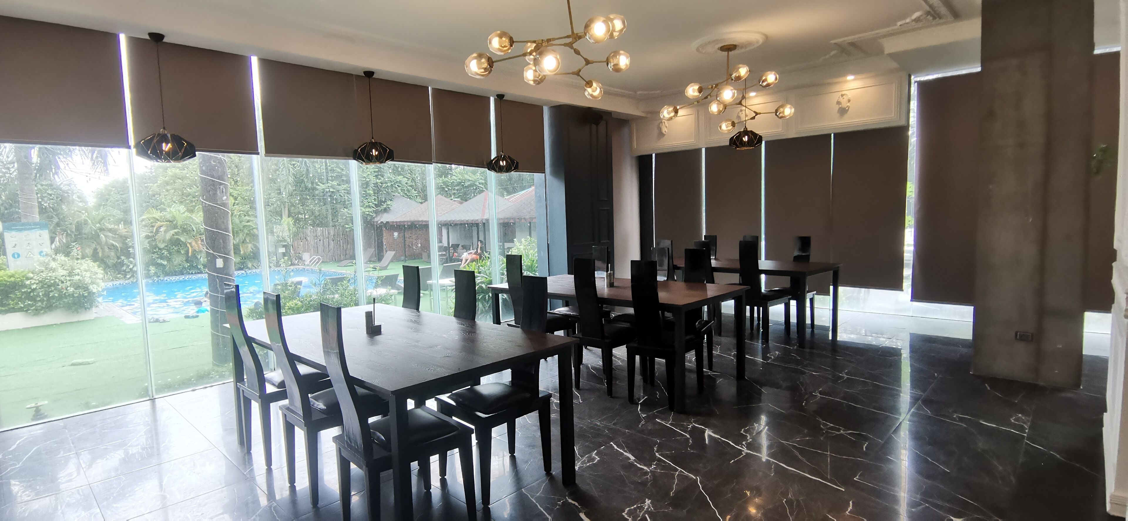 Un comedor amplio con ventanas grandes, candelabros modernos y vistas a una piscina y zonas verdes.