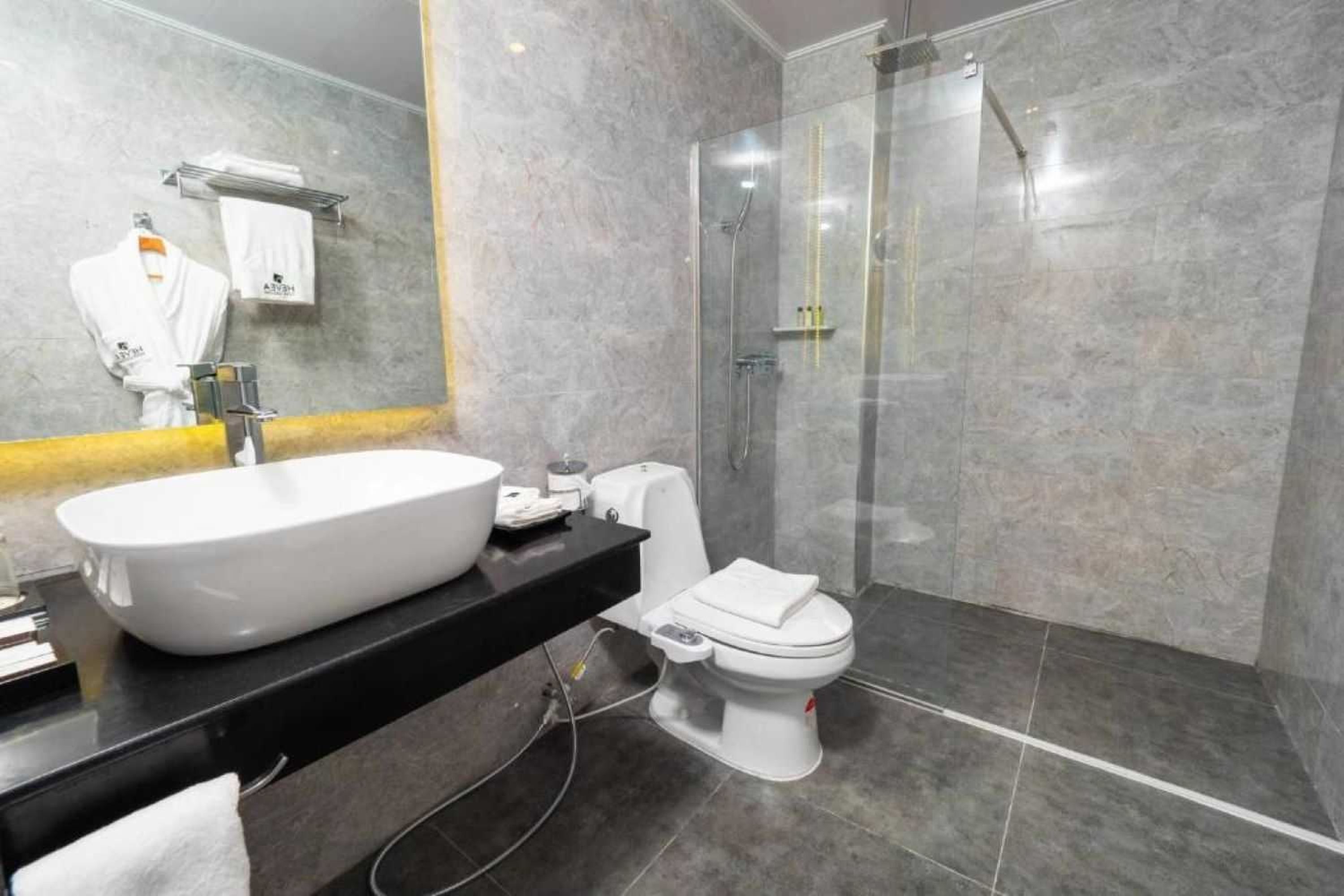 A modern bathroom with a large white sink, a toilet, and a glass-enclosed shower.