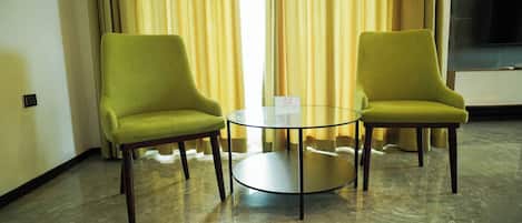 Una habitación con dos sillones verdes, una mesa de vidrio y un televisor montado en la pared.