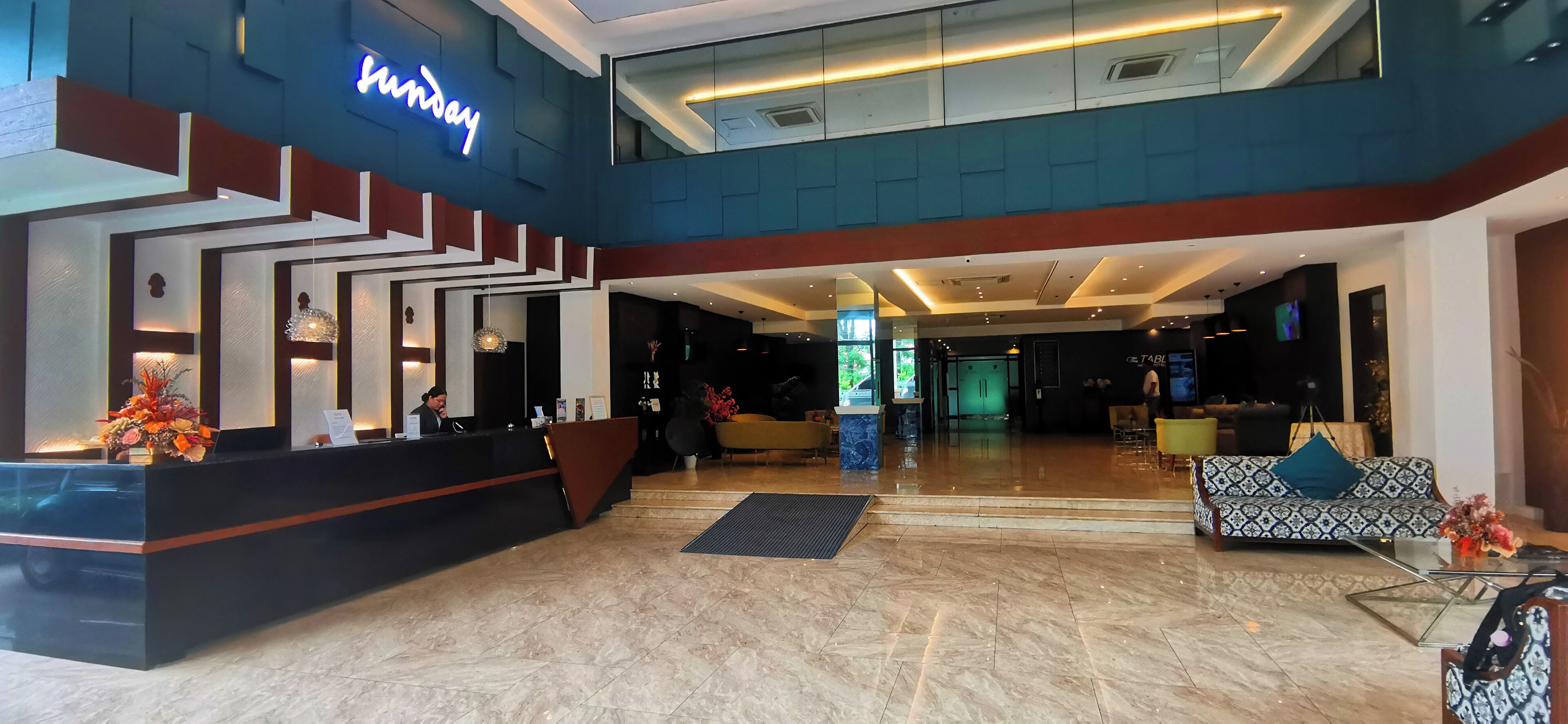 Un vestíbulo de hotel con una recepción, una escalera, un sofá y una pantalla de televisión.