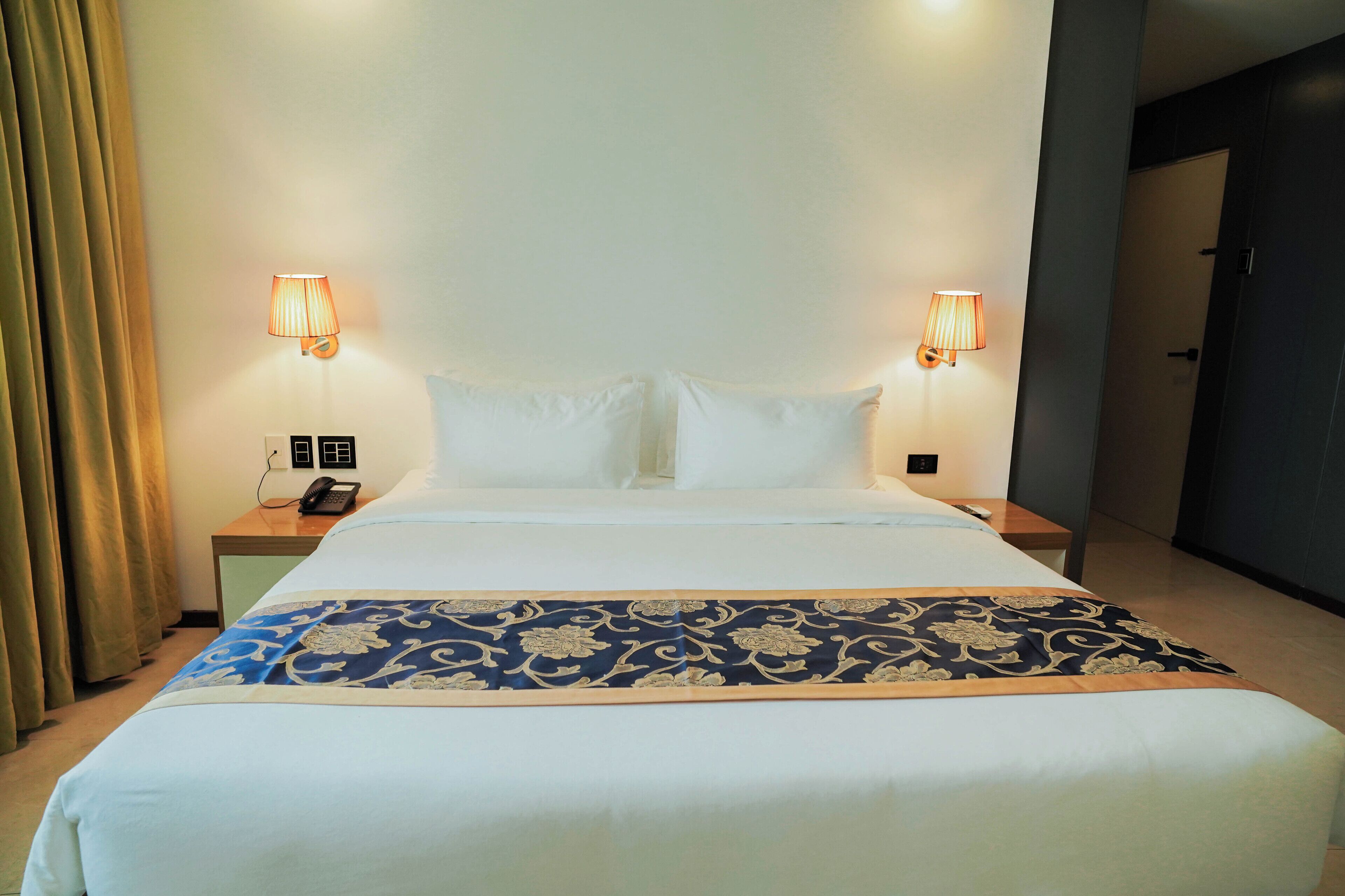 Habitación de hotel con una cama grande, dos lámparas de noche, un teléfono y una puerta a la derecha.