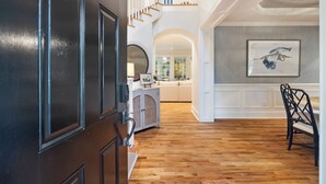 Um corredor amplo com piso de madeira, uma escada e um espaço de jantar com mesa e cadeiras.