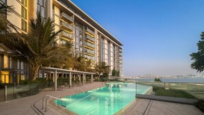 A swimming pool with a glass barrier, a covered seating area, and a view of a city skyline.