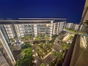Un hôtel moderne à plusieurs étages, doté d’une cour intérieure agrémentée de palmiers et d’une façade bien éclairée.