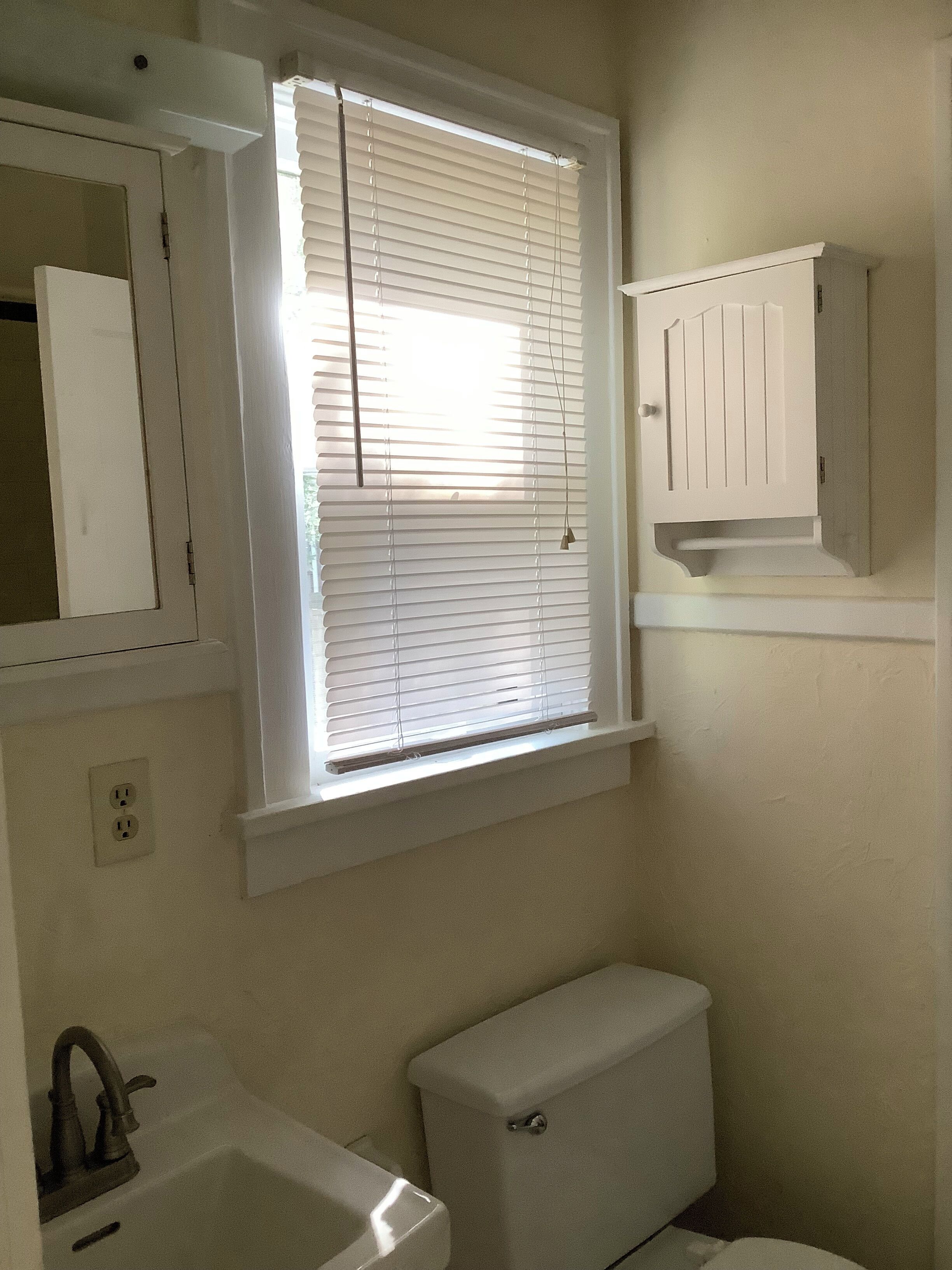 Un baño con inodoro, lavamanos y ventana con persianas.