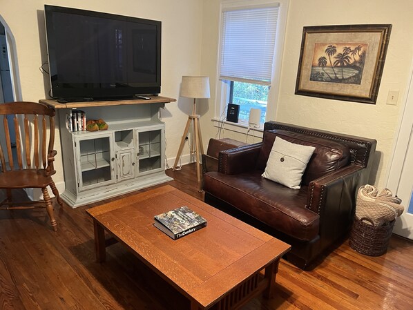 A living room with a wooden coffee table, a brown leather sofa, a television on a stand, a white cabinet, and a framed picture on the wall.