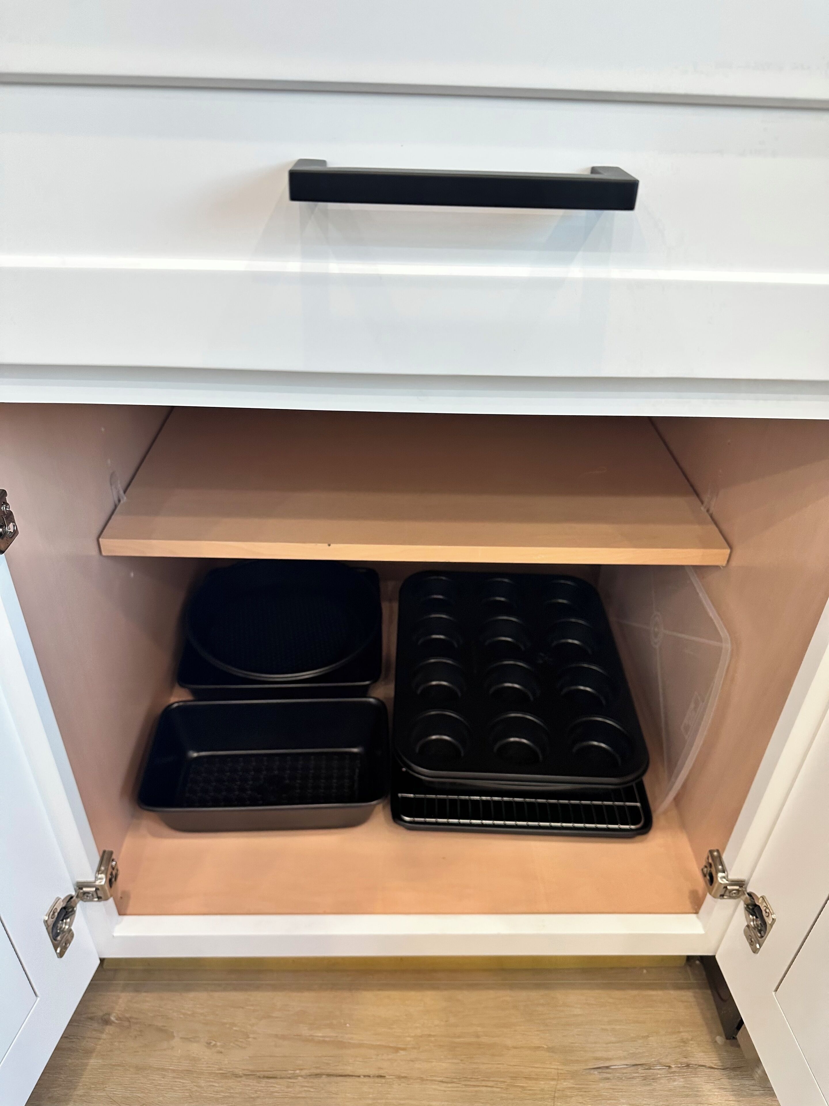 A kitchen cabinet with a pull-out shelf containing baking trays and a griddle.
