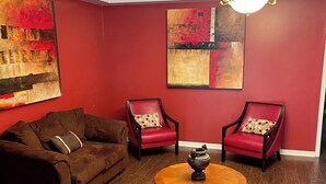 Een woonkamer met een bruine bank, twee rode fauteuils, een houten salontafel en twee abstracte schilderijen aan de wanden.