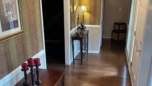 Een gang met behang met patroon, een houten vloer, een tafel met kaarsen, een lamp en een spiegel.