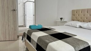 Un dormitorio con cama, mesita de noche, ventana y puerta.