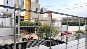 Un edificio moderno con balcón de cristal, barandillas de metal y un coche rojo estacionado afuera.
