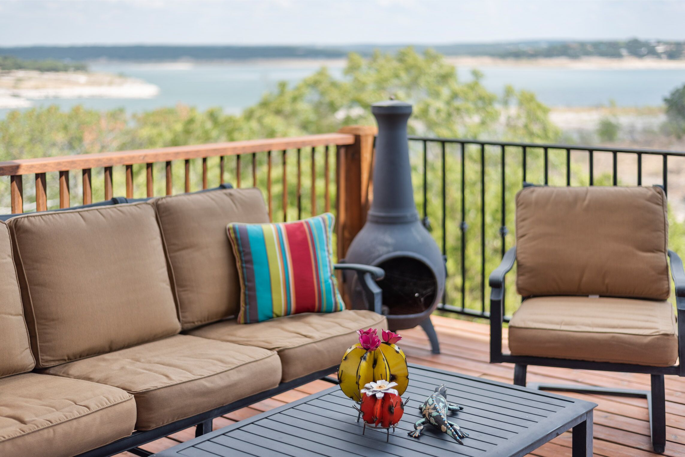 A deck with a sofa and armchair, a table with decorative items, and a view of a body of water and greenery.