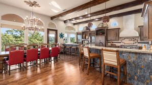 A spacious kitchen with wooden beams, a dining area with red chairs, and a large island with a stone backsplash. - Riviera Paradise | Lake Access (Canyon Lake)