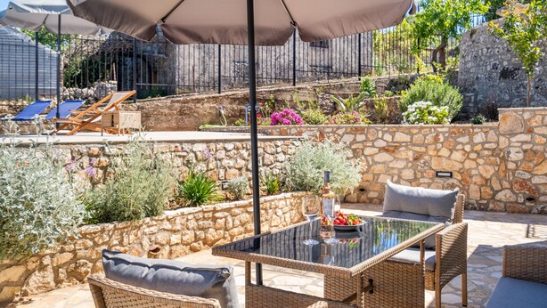 An outdoor patio with wicker furniture, a glass table, and a stone wall. - Villa 'Milia's House' with Sea View, Wi-Fi and Air Conditioning (Ithaca)