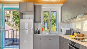 A modern kitchen with grey cabinets, a white refrigerator, and a window overlooking a garden. - Villa 'Milia's House' with Sea View, Wi-Fi and Air Conditioning (Ithaca)