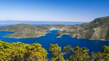A coastal landscape with clear blue waters, green hills, and dense tree coverage.