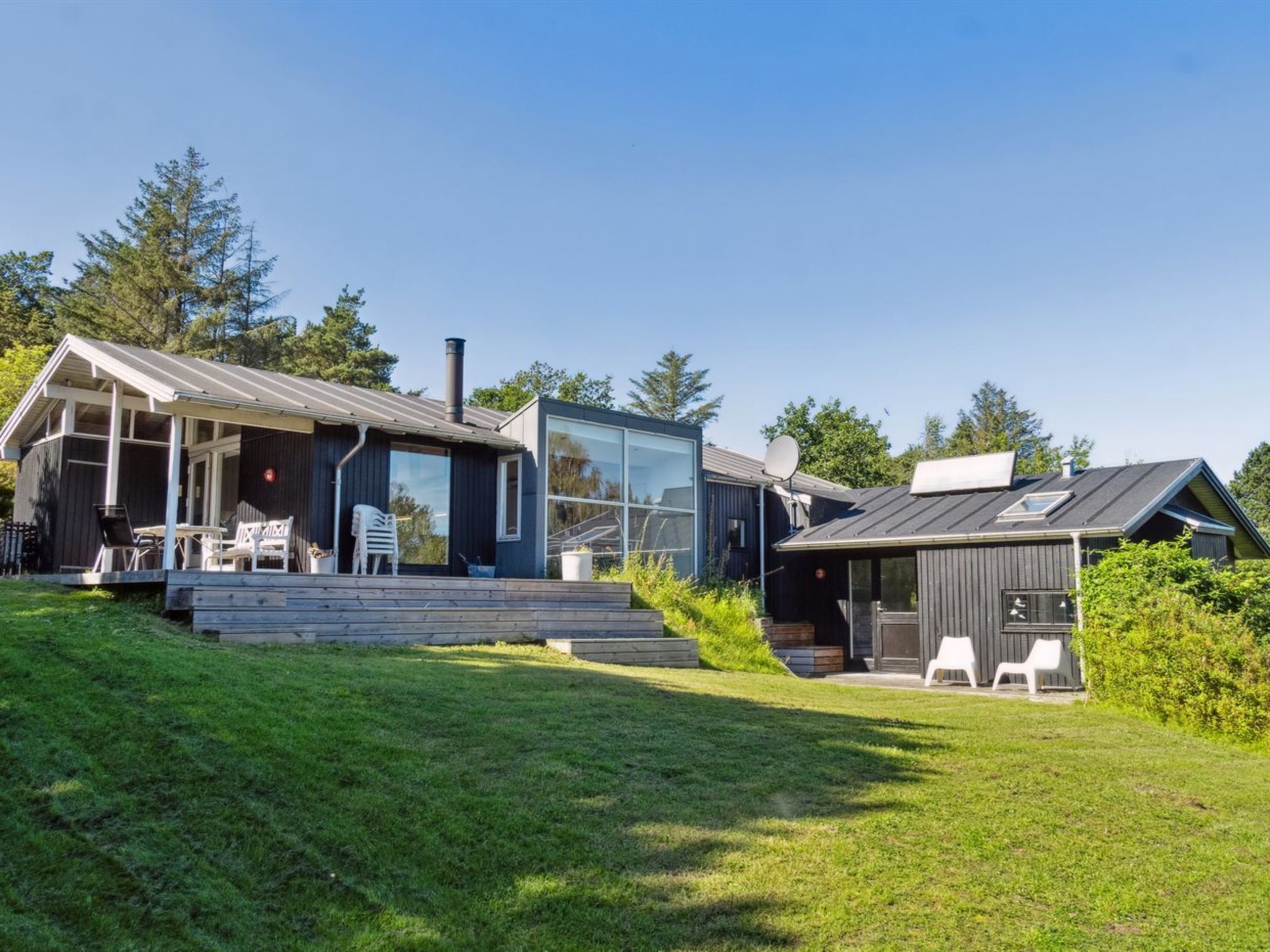 A modern house with a large glass window, a deck with outdoor furniture, and a chimney.