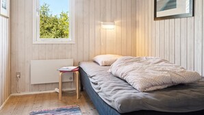 Een slaapkamer met een bed, een raam, een nachtkastje en een wandlamp.