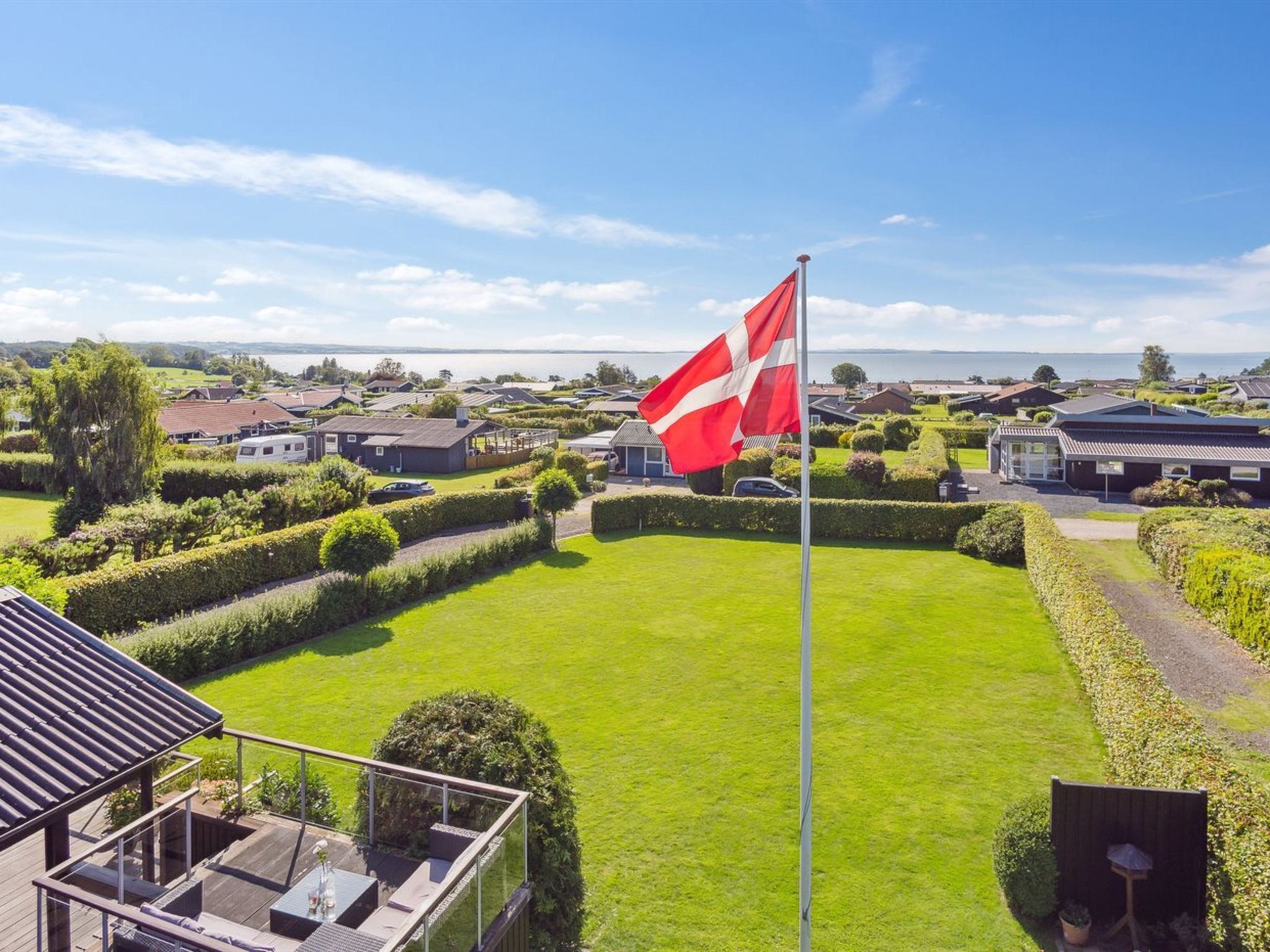 A residential area with a flag, neatly trimmed hedges, and a clear view of the sea.